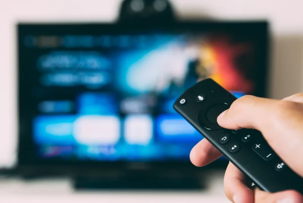 A person holds a TV remote in from of a screen